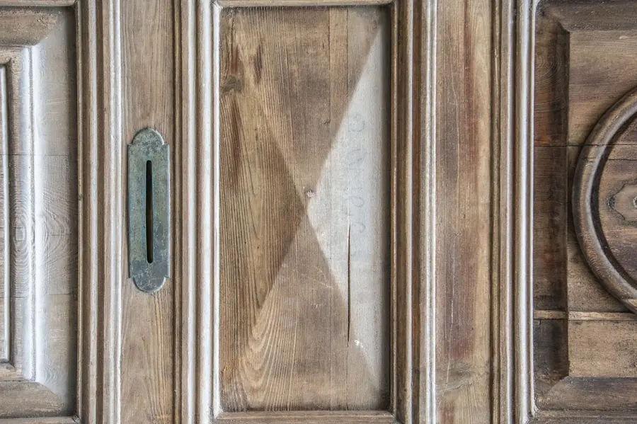 Weathered wood-panelled door with a tarnished brass letter plate, the kind you would find on an old bank's back office